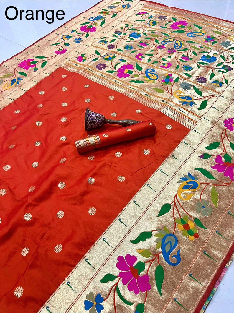 May include: An orange sari with a floral and paisley design. The border features gold trim and colorful flowers. The word "Orange" is in the top left corner. A decorative item is on the sari.
