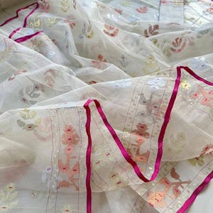 May include: A sheer white fabric with a floral pattern in pastel colors. The edges are trimmed with a bright pink ribbon. The fabric is likely a scarf or shawl, with a delicate and airy appearance.
