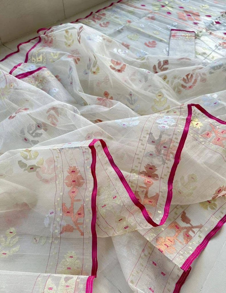 May include: A sheer white fabric with a floral pattern in pastel colors. The edges are trimmed with a bright pink ribbon. The fabric is likely a scarf or shawl, with a delicate and airy appearance.