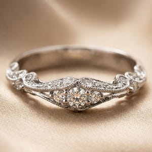 May include: A silver ring with a delicate, ornate design. The ring features a row of three central stones, surrounded by smaller accent stones and intricate filigree detailing. The ring is set against a neutral background.
