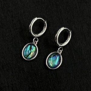 May include: A pair of silver-toned hoop earrings featuring dangling oval-shaped charms. Each charm contains an iridescent abalone shell inlay displaying vibrant shades of blue, green, and purple with a polished metallic border and secure clasp.