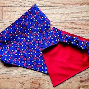 May include: Two dog bandanas. One is blue with a pattern of white stars and red flowers. The other is red with a blue patterned trim. The bandanas are made of fabric.