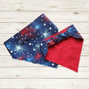 May include: Two patriotic bandanas. One is navy blue with a white star and red and blue firework design. The other is red with a textured pattern. The bandanas are likely for a pet.