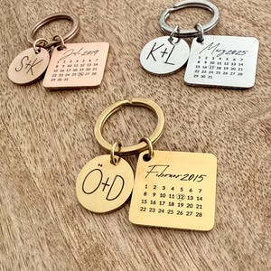 Könnte beinhalten: Drei personalisierte Schlüsselanhänger mit eingravierten Initialen und Daten. Einer ist roségoldfarben mit "S+K" und "Jul-2019". Ein weiterer ist silberfarben mit "K+L" und "May 2025". Der dritte ist goldfarben mit "Ö+D" und "Februar 2015".