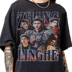 May include: A charcoal gray short-sleeve t-shirt featuring a graphic print of five portraits of the same person in various outfits. The text ZHANG is printed in large white letters at the top and LINGHE is printed in large white letters at the bottom.