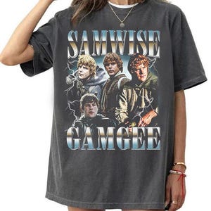 May include: A charcoal grey short-sleeve t-shirt featuring a graphic print of Samwise Gamgee from The Lord of the Rings. The design includes the text SAMWISE GAMGEE in a metallic blue and white gradient font, surrounded by lightning bolt imagery.