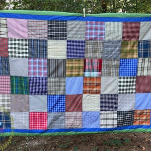 Könnte beinhalten: Eine Patchwork-Decke aus Quadraten aus verschiedenen karierten Stoffen in Blautönen, Grün, Rot und Braun. Die Decke ist mit einem grünen und blauen Rand versehen.