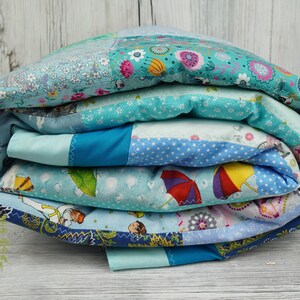 Puede incluir: Una colcha de retazos azul y blanca enrollada con una variedad de patrones, incluyendo flores, lunares y paraguas. La colcha está hecha de tela suave y cómoda, perfecta para acurrucarse en el sofá.