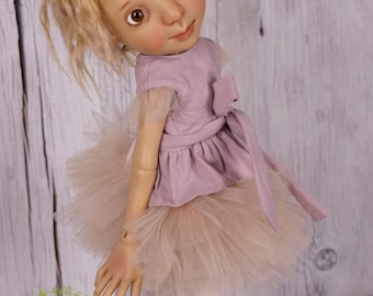 May include: A porcelain doll with blonde hair wearing a light pink dress and a tulle tutu. The doll is wearing white tights and pink ballet shoes.