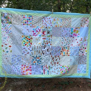 Peut inclure: Une courtepointe en patchwork avec une bordure bleu clair et une bordure intérieure vert clair. La courtepointe est composée de nombreux carrés de tissu différents, chacun avec un motif différent. Les motifs comprennent des animaux, des formes géométriques et des lettres.