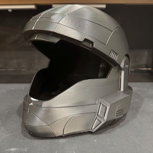 May include: A grey, futuristic helmet with a wide visor opening. The helmet has a smooth, metallic appearance with angular design elements and a dark interior. The overall aesthetic suggests a science fiction or cosplay theme.