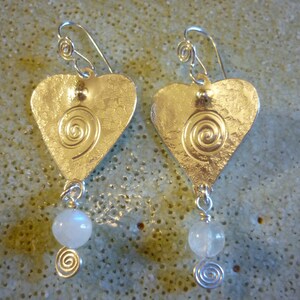 Puede incluir: Pendientes de plata en forma de coraz&oacute;n con un dise&ntilde;o en espiral y un colgante de cuentas blancas.