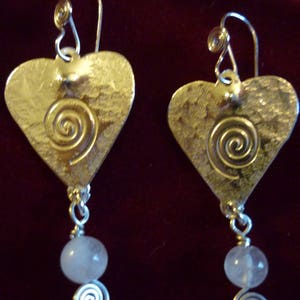 Puede incluir: Un par de pendientes de plata en forma de coraz&oacute;n con un dise&ntilde;o de espiral y un colgante de piedra rosa.