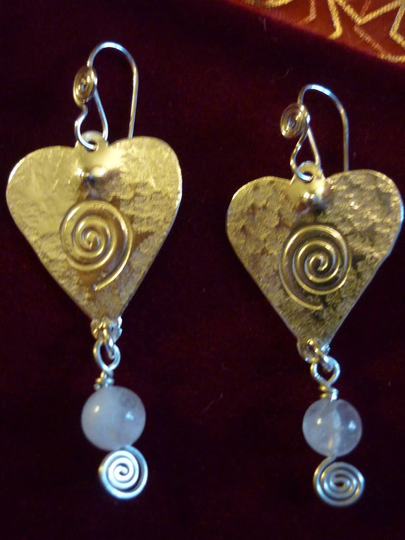 Puede incluir: Un par de pendientes de plata en forma de coraz&oacute;n con un dise&ntilde;o de espiral y un colgante de piedra rosa.