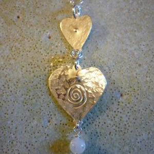 Puede incluir: Collar de plata con tres colgantes en forma de coraz&oacute;n. El coraz&oacute;n inferior tiene un dise&ntilde;o en espiral y est&aacute; unido a una cuenta blanca.