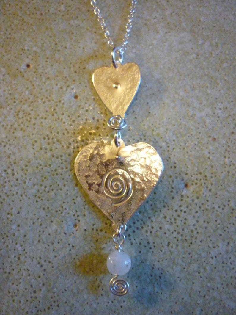Puede incluir: Collar de plata con tres colgantes en forma de coraz&oacute;n. El coraz&oacute;n inferior tiene un dise&ntilde;o en espiral y est&aacute; unido a una cuenta blanca.