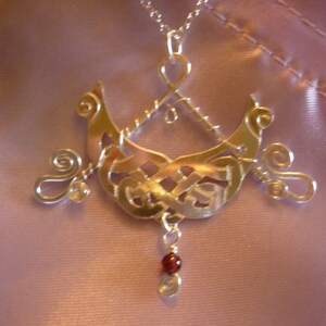 Puede incluir: Collar de plata con un colgante detallado e intrincado con un diseño de nudo y una piedra preciosa roja colgante.