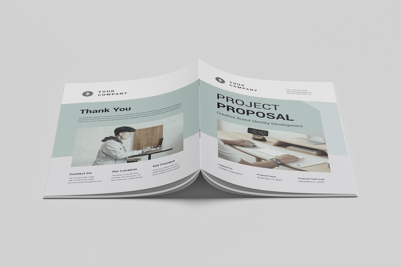 May include: Open brochure with the text "PROJECT PROPOSAL" and "Thank You". The brochure has a light blue and white design. The brochure includes images of people working on computers.