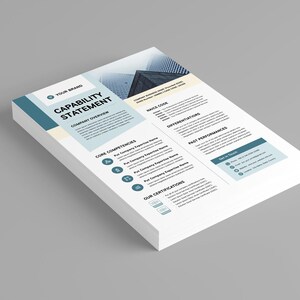May include: A stack of white Capability Statement documents with teal and light blue accents. The document includes sections for company overview, core competencies, and past performances. The background is a solid gray.