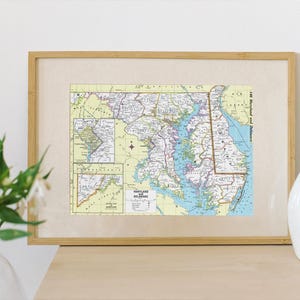 May include: A framed vintage map of Maryland and Delaware with a light yellow background and blue and green accents. The map shows major roads and cities.