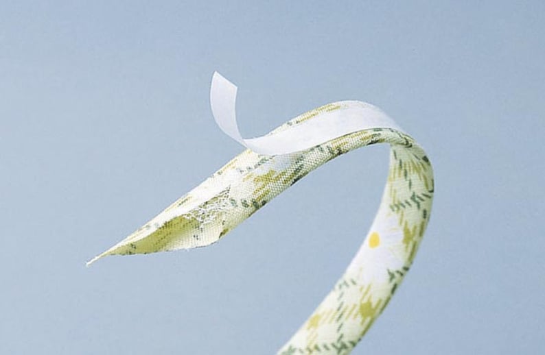 May include: A white fabric tape with adhesive backing, partially peeled back to reveal the adhesive. The fabric has a floral pattern in shades of green and yellow.