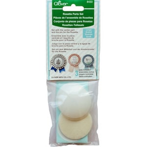 May include: A package of three sets of rosette parts for crafting. The package includes white and cream felt circles, a pin, and a center piece. The package is labeled "Rosette Parts Set" and "Large/Grand/Grande/Groß".