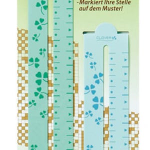 May include: A set of two light teal pattern chart markers with a clover design. The markers have a ruler-like appearance with measurement markings and a slot down the center. The packaging includes text in multiple languages, including "Pattern Chart Marker Set."