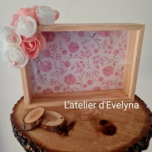 Könnte beinhalten: Ein Holzschattenkasten mit floral gemustertem Innenraum und einer Ansammlung rosa und weißer Blumen in der oberen linken Ecke. Die Box wird auf einer Holzbaumscheibe präsentiert. Der Text "L'atelier d'Evelyna" ist sichtbar.
