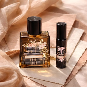 May include: A perfume bottle and rollerball set. The perfume bottle is rectangular with a black cap and a floral and book design. The rollerball is black with a matching design. The background is a soft, neutral color.