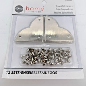 May include: A package of 12 sets of silver quatrefoil corners with 12 sets of silver tacks. The package is labeled "Quatrefoil Corners, Coins de quadrilobes, Esquinas de Cuadrifolio" and "12 SETS/ENSEMBLES/JUEGOS".