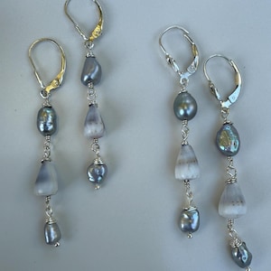 以下が含まれることがあります： グレーと白の石とグレーのパールが特徴の、シルバーのぶら下がりピアス。ピアスはレバーバック留め具で、シルバーワイヤーで繋がれています。ユニークなアクセサリーです。
