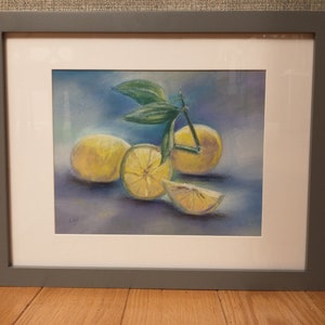 May include: A framed pastel artwork featuring lemons. The painting depicts whole and sliced lemons with green leaves against a blue and purple background. The artwork is framed in a gray frame with a white mat.