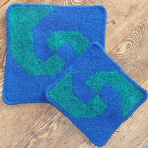 Puede incluir: Dos agarraderas de olla de punto azul con un diseño de espiral verde.