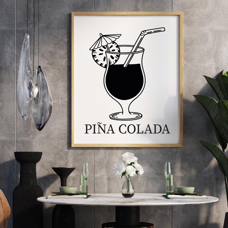 May include: A framed black and white illustration of a Pi&ntilde;a Colada cocktail. The image features a tall glass with a straw, a pineapple slice, and a small umbrella. The words "PI&Ntilde;A COLADA" are printed below the image.