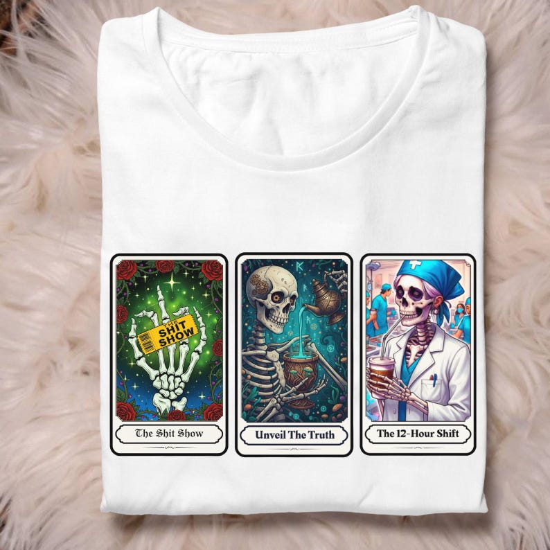 Puede incluir: Camiseta blanca con tres dise&ntilde;os de cartas del tarot. Las cartas muestran ilustraciones de esqueletos con las frases "The Shit Show", "Unveil The Truth" y "The 12-Hour Shift". La camiseta est&aacute; doblada limpiamente.