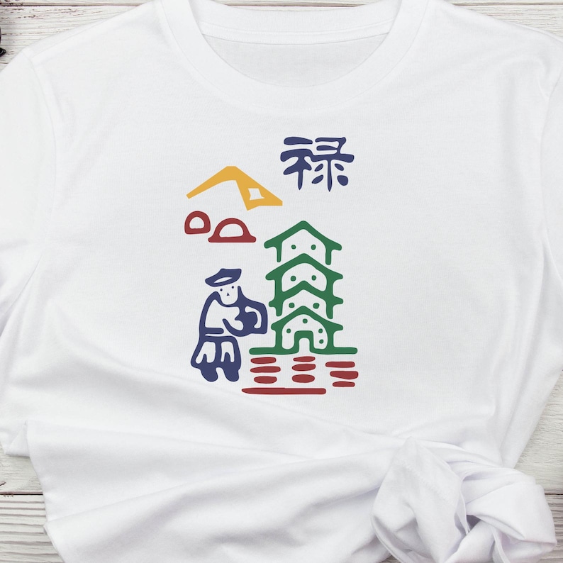 May include: White t-shirt with a colourful graphic design. The design features a stylized illustration of a person, buildings, and other shapes in blue, green, red, yellow, and brown. The shirt has a crew neck.