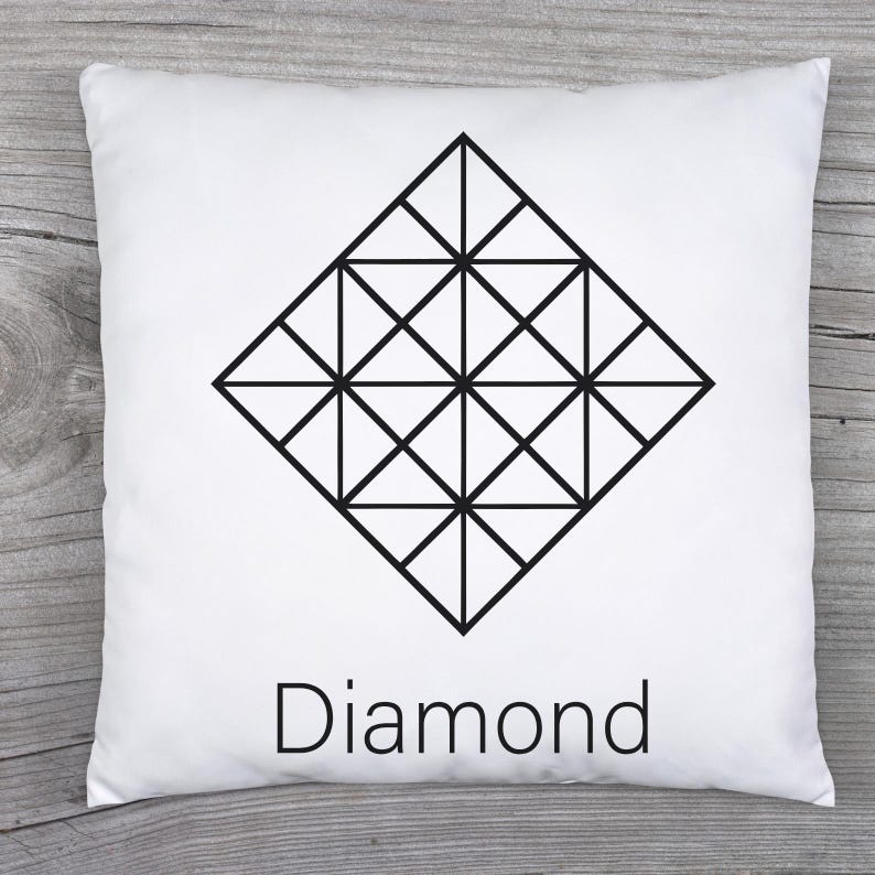 May include: White square pillow with a black geometric diamond design. The word "Diamond" is printed in black below the design. The pillow is on a wooden surface.