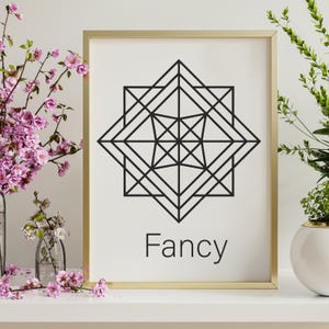 May include: A framed print with a gold border features a black geometric design on a white background. The word "Fancy" is printed in black at the bottom. The print is displayed on a white surface with pink flowers.