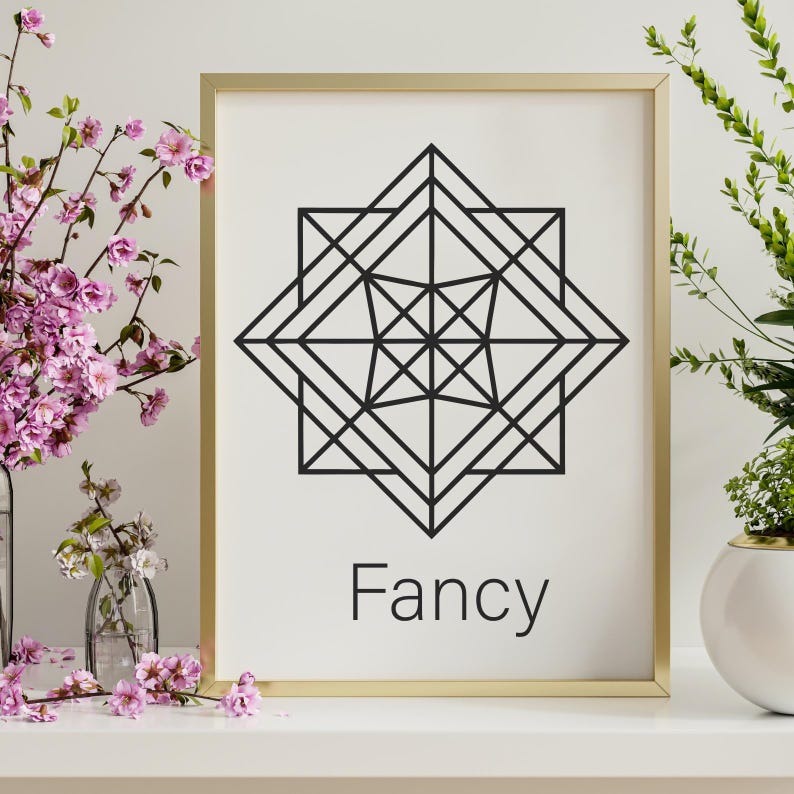 May include: A framed print with a gold border features a black geometric design on a white background. The word "Fancy" is printed in black at the bottom. The print is displayed on a white surface with pink flowers.