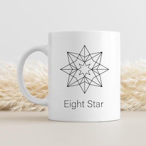 May include: White ceramic mug featuring a black geometric eight-pointed star design. The words "Eight Star" are printed below the star. The mug has a curved handle and is suitable for hot or cold beverages.