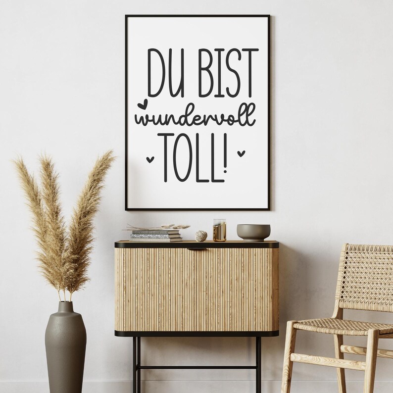 K&ouml;nnte beinhalten: Ein gerahmter Druck mit den schwarzen Worten &bdquo;DU BIST wundervoll TOLL!&ldquo; auf wei&szlig;em Hintergrund. Der Druck wird &uuml;ber einem Holzschrank mit einer Vase mit getrockneten Pflanzen, einer kleinen Sch&uuml;ssel und einem Stuhl angezeigt.