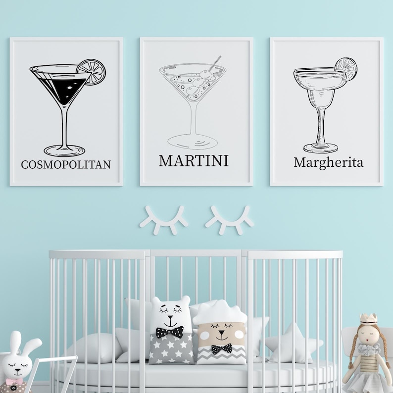 May include: Three framed black and white cocktail prints: Cosmopolitan, Martini, and Margherita. The prints are displayed above a white crib in a nursery with a light blue wall. Decorative pillows and a doll are in the crib.