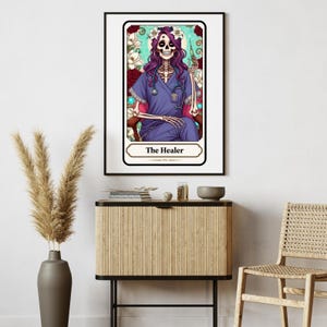 Puede incluir: Una impresi&oacute;n enmarcada que presenta un esqueleto con uniforme m&eacute;dico, un estetoscopio y una jeringa, etiquetada como "The Healer". La obra de arte tiene un fondo floral con una combinaci&oacute;n de colores turquesa y rojo. El esqueleto tiene pelo morado y una corona de flores.