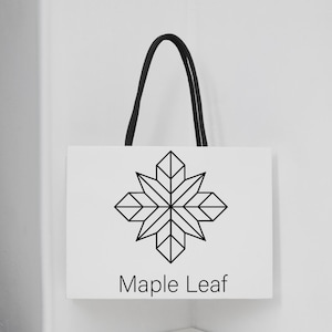 May include: White shopping bag with a black geometric maple leaf design and the words "Maple Leaf" in a simple font. The bag has a black rope handle.