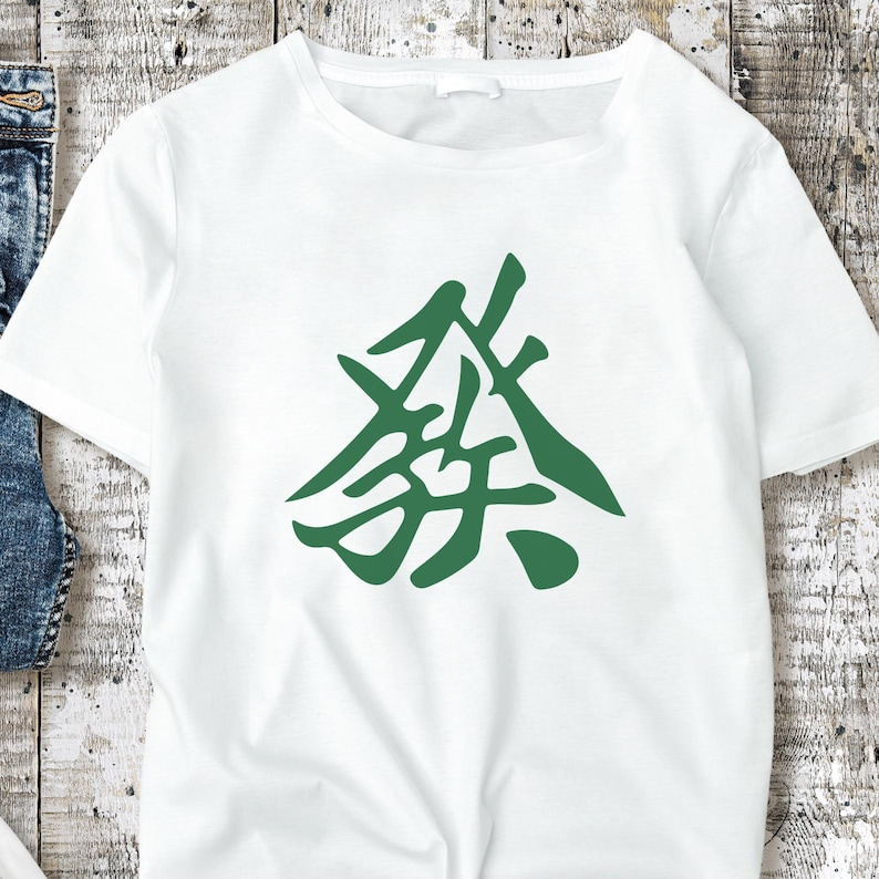 May include: A white t-shirt with a green graphic. The design is an abstract symbol. The t-shirt is made of a soft material, likely cotton. The graphic is positioned centrally on the front of the shirt.