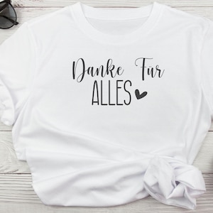 K&ouml;nnte beinhalten: Ein wei&szlig;es T-Shirt mit dem deutschen Schriftzug "Danke F&uuml;r ALLES" in schwarzer Schrift, begleitet von einem kleinen Herzsymbol. Das Shirt besteht aus einem weichen Material und hat einen klassischen Rundhalsausschnitt.