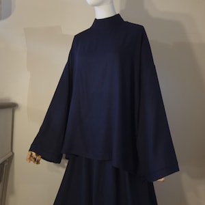 May include: A solid dark navy blue two-piece outfit consisting of a loose-fitting top with a high mock neckline and wide, long sleeves, paired with a matching floor-length skirt. The ensemble features a clean, unpatterned fabric design.