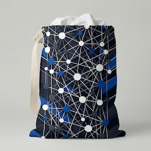 Può includere: Un sacco per la biancheria blu scuro con un motivo geometrico bianco, blu e grigio. La borsa ha una chiusura con coulisse e un cinturino in tela beige. La borsa è riempita di tessuto bianco.