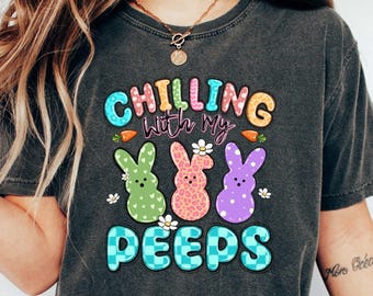 May include: A gray t-shirt with the text "Chilling with my Peeps" in colorful letters. The text is surrounded by three cartoon Peeps, each with a different color and pattern.