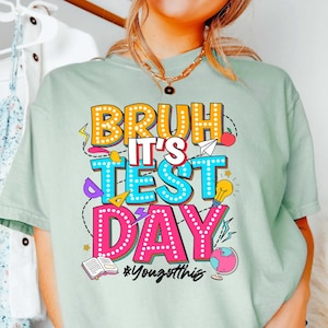 May include: A light green t-shirt with a colorful graphic that says "Bruh it's test day" with a hashtag that says "#YouGotThis".